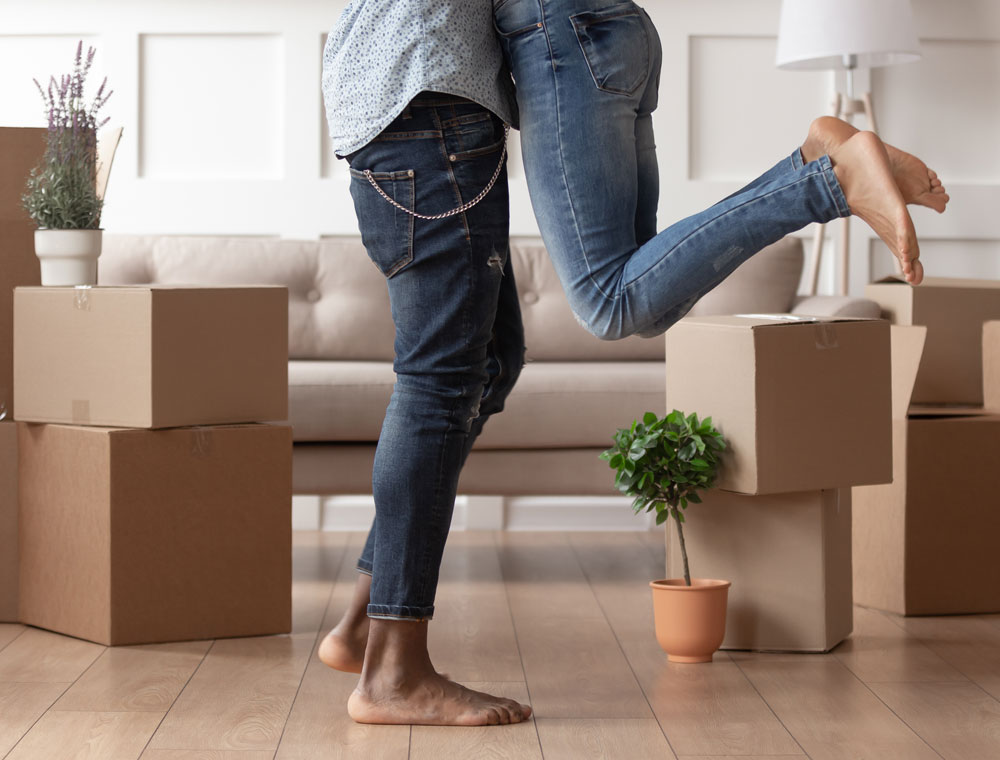 Couple moving into a new home - man picking up woman in excitement with moving boxes