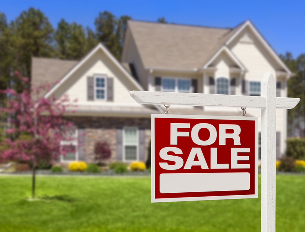 For Sale sign in foreground with a blurred home in the background