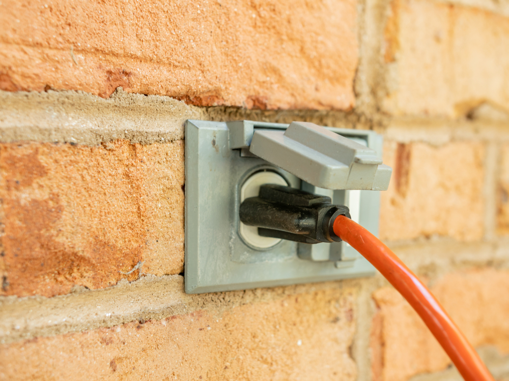 Power cord plugged into outdoor electrical wall socket with incorrect outlet cover