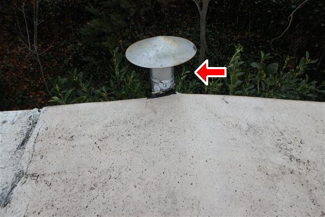 Picture of a flue that is too close to the roof. A red arrow points to the flue shaft to show distance.