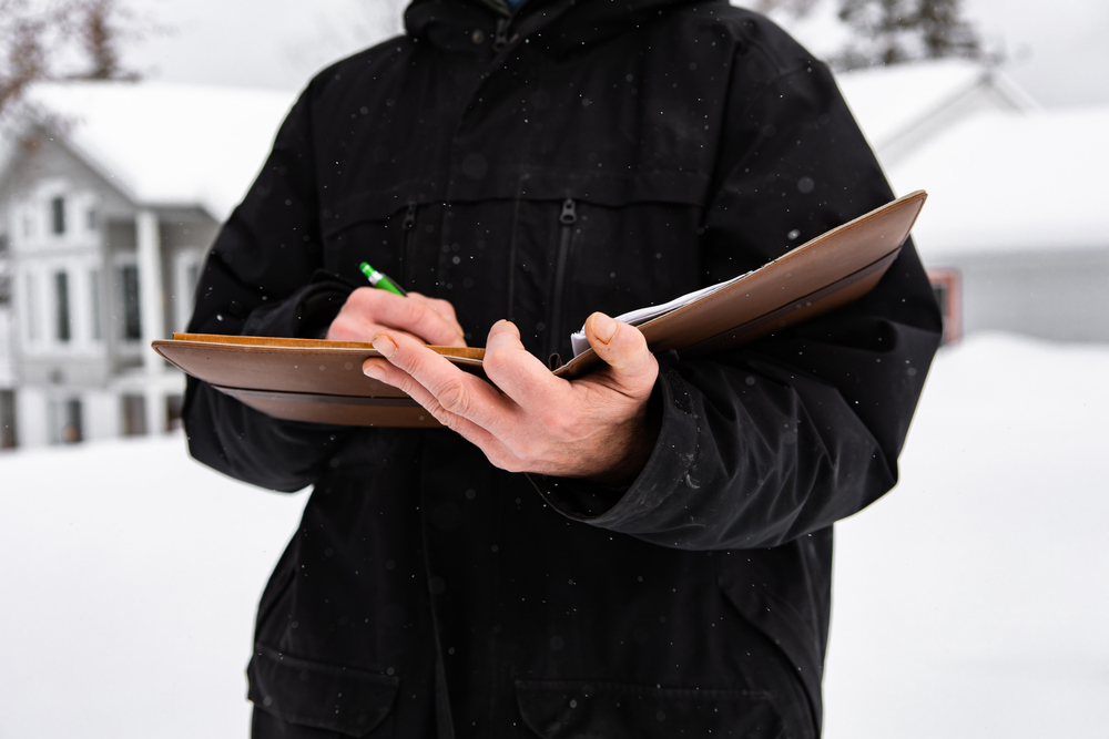 man standing outside during home inspection in winter. he wearing a cold winter black jacket as he taking notes on notebook