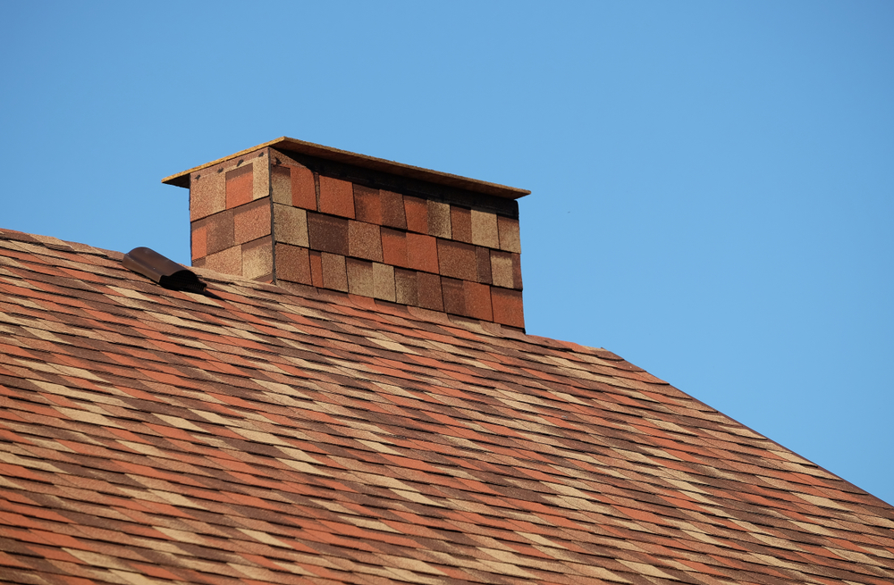 Part of brown roof of a house covered with soft shingles with short chimney