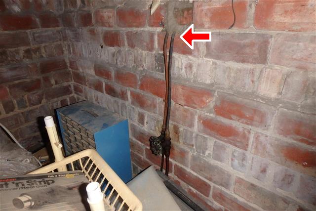 basement brick wall with oil lines coming out it which may indicate a buried oil tank in the wall