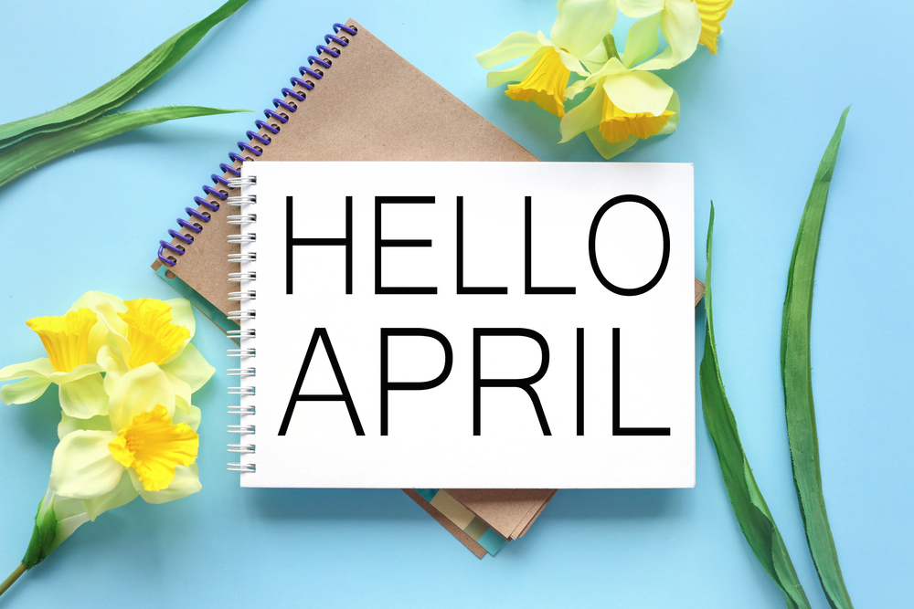 Hello April text on white notepad paper on blue background near yellow flowers and green leaves
