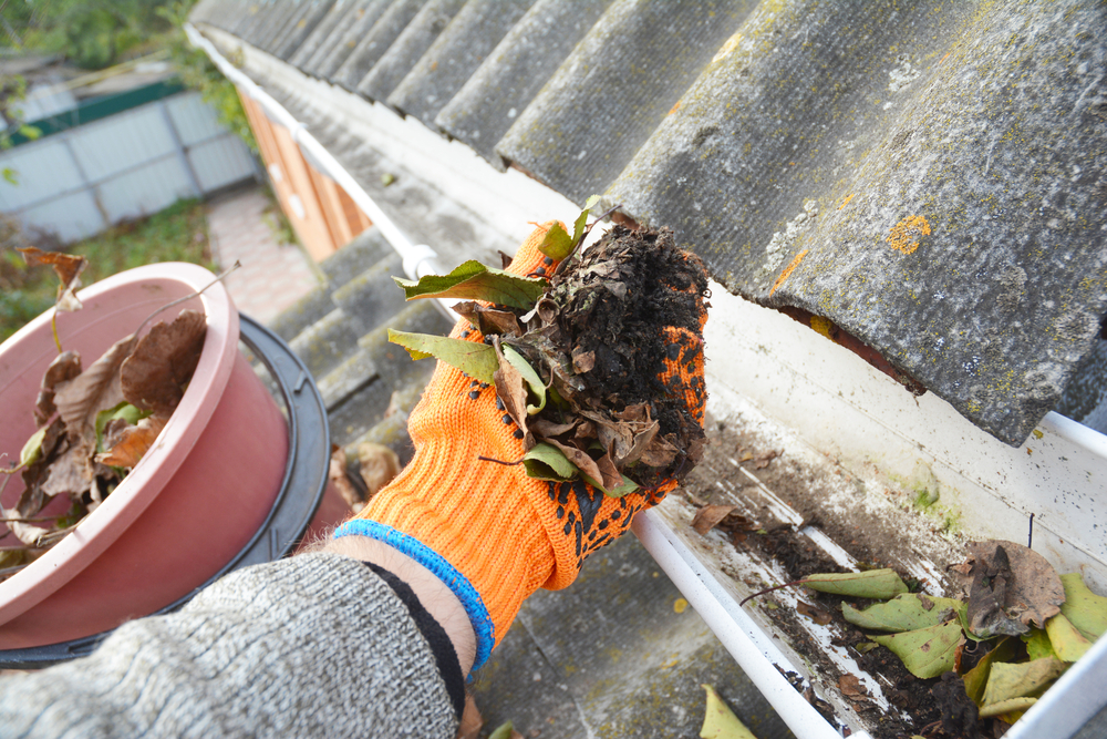 homeowner cleaning gutters of debris with gloves on