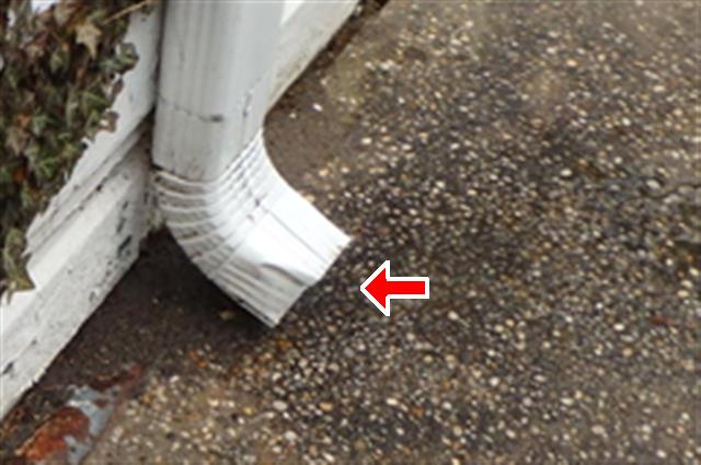 picture from a home inspection report of a short downspout without an extension. Red arrow points to the end of the downspout.