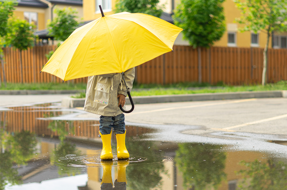 A child holds a yellow umbrella standing in a puddle outside.