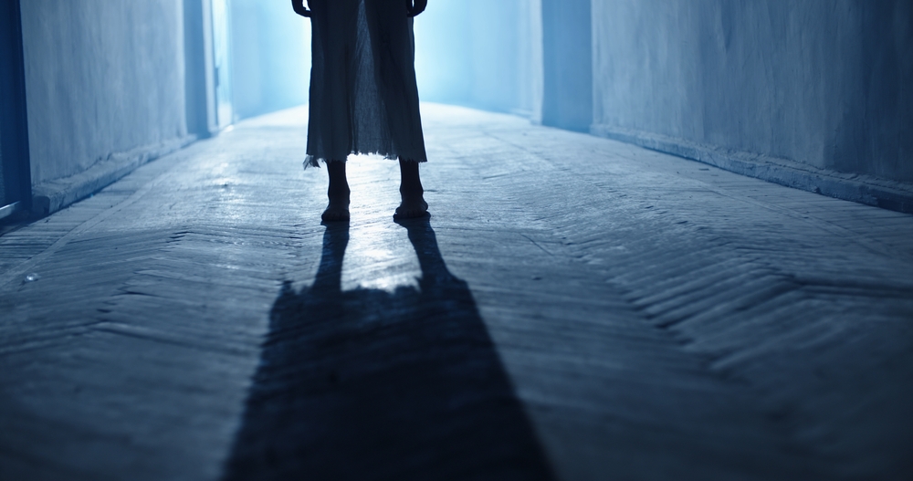 Low angle shot of legs of little girl ghost slowly creeping on floor of hallway of old abandoned haunted house - horror scene, horror movie